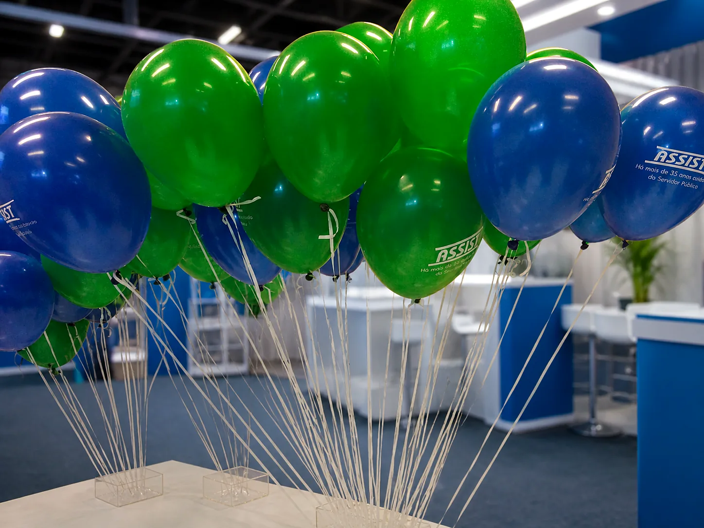 Balões azuis e verdes personalizados em estande de evento corporativo